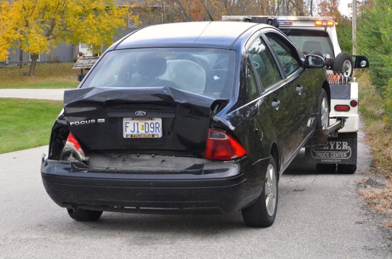Wheel Lift Tow Truck Hauling A Damaged Black Car